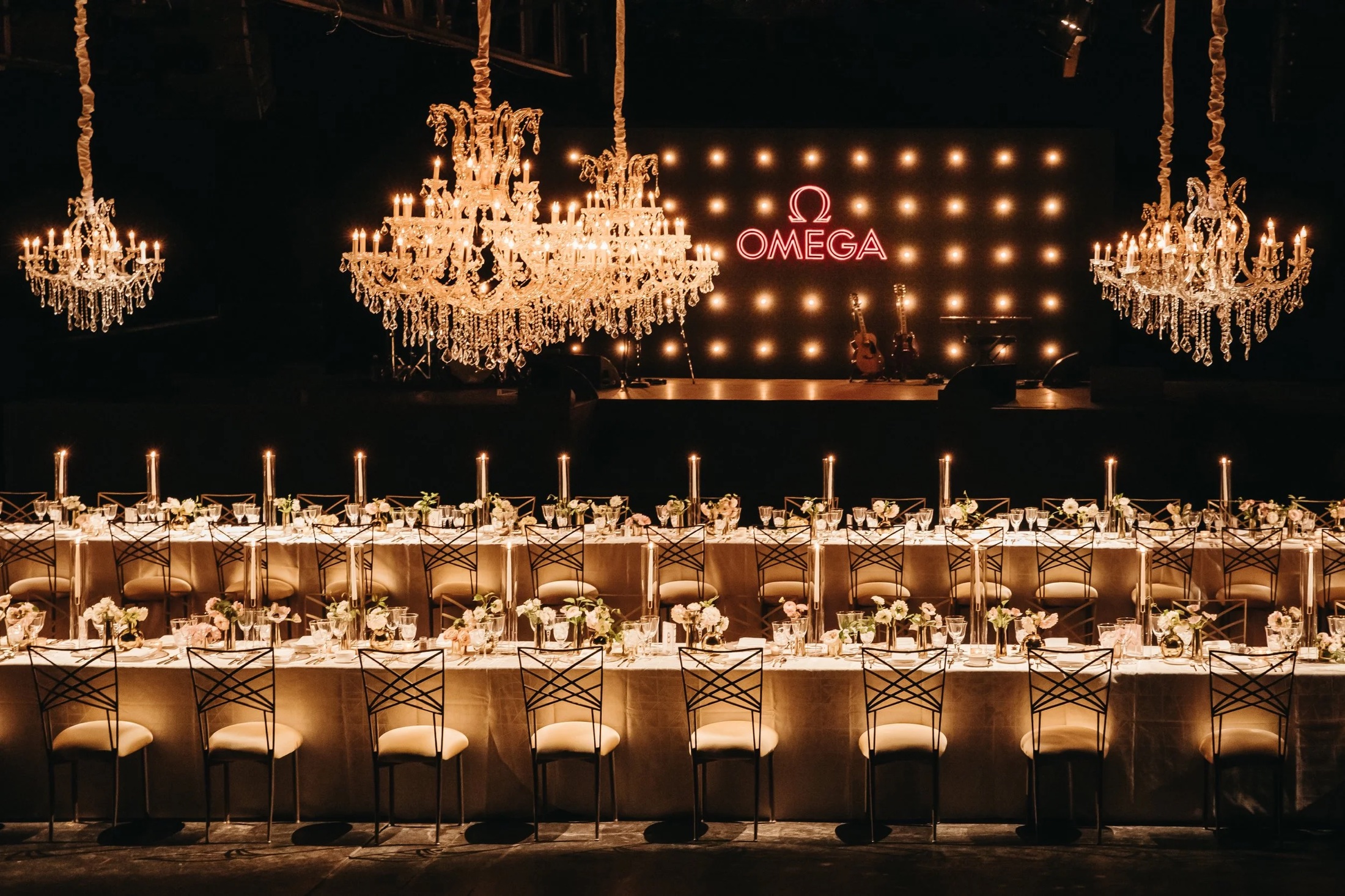 A long candlelit dinner table under crystal chandeliers at a brand evening