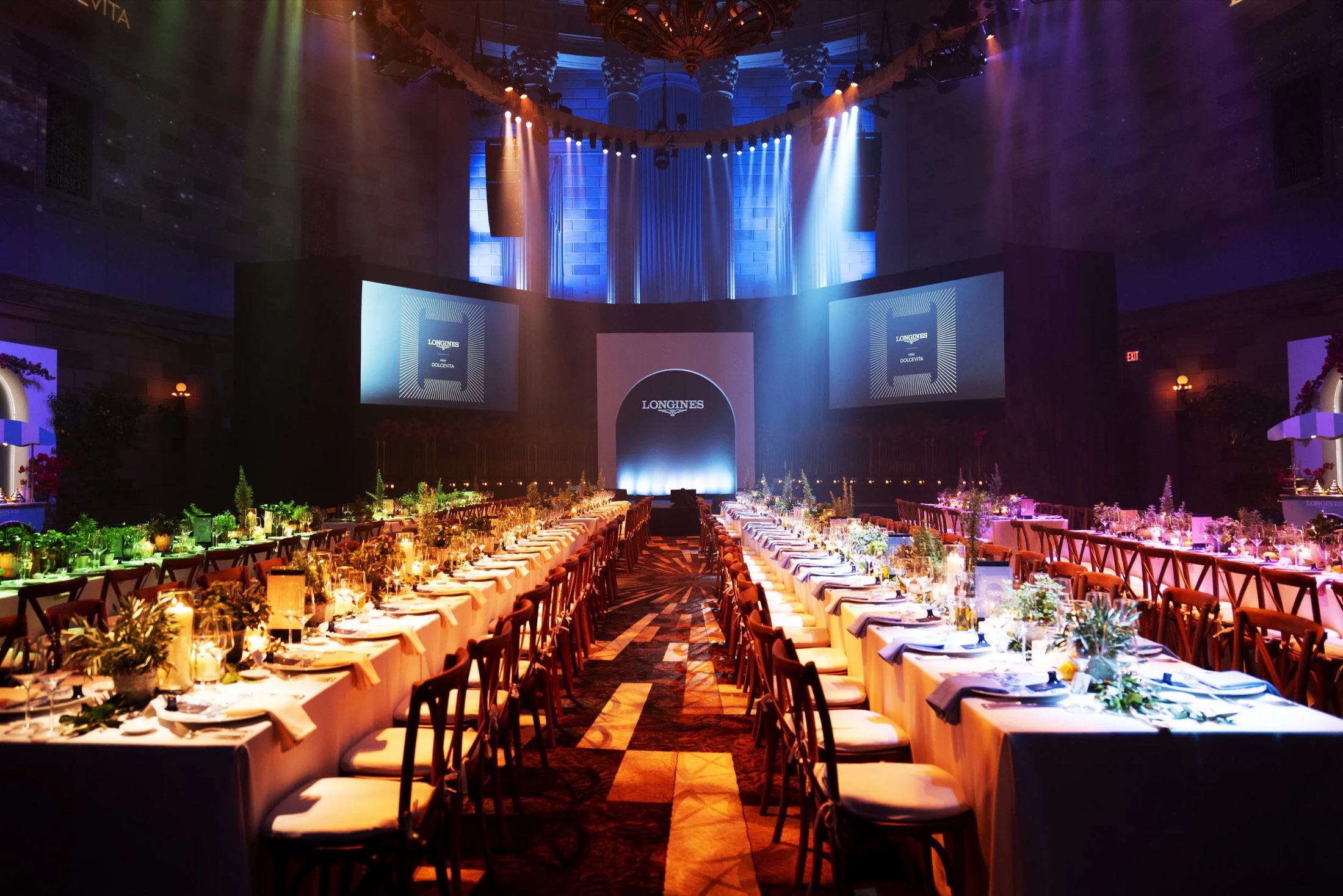 Long dinner tables in a vaulted hall lit for a watch brand evening