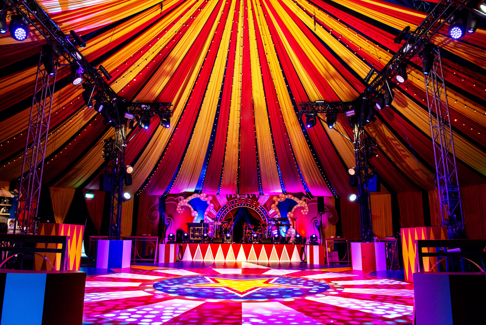A circus big top dressed in red and gold with a lit stage and dance floor