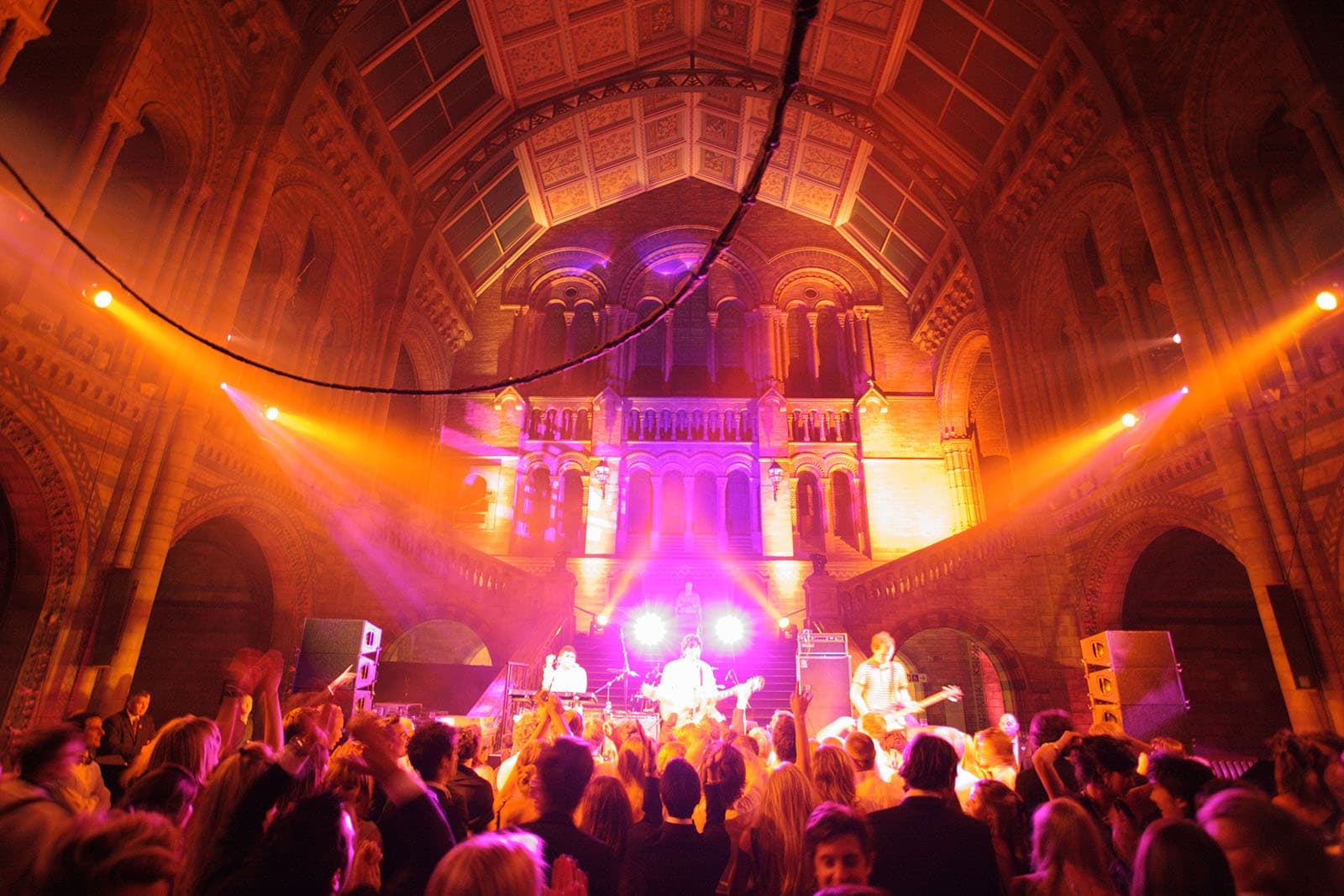 A live band on a lit stage in a historic hall packed with guests